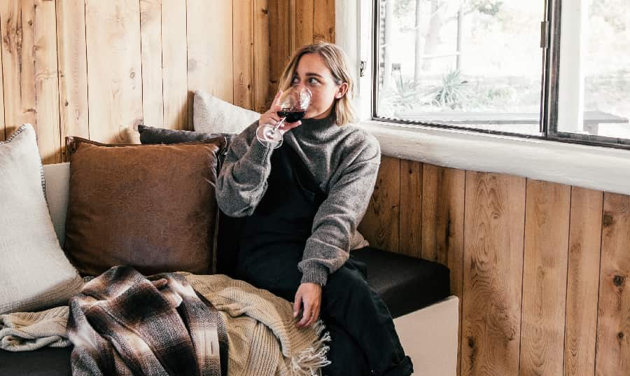 A woman seated on a couch, sipping wine, eyes reflecting her intent to conquer her nightly drinking habit.