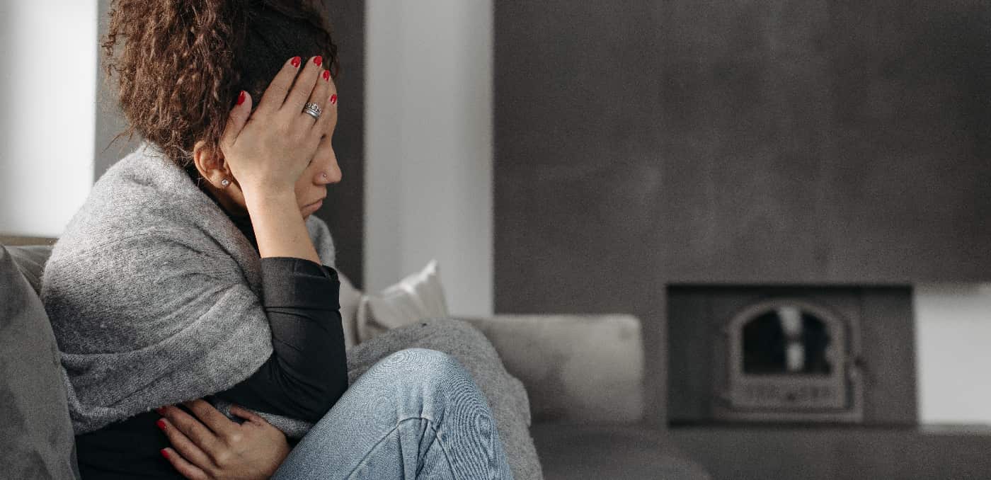 Woman on couch grappling with symptoms of precipitated withdrawals, holding her head in discomfort.