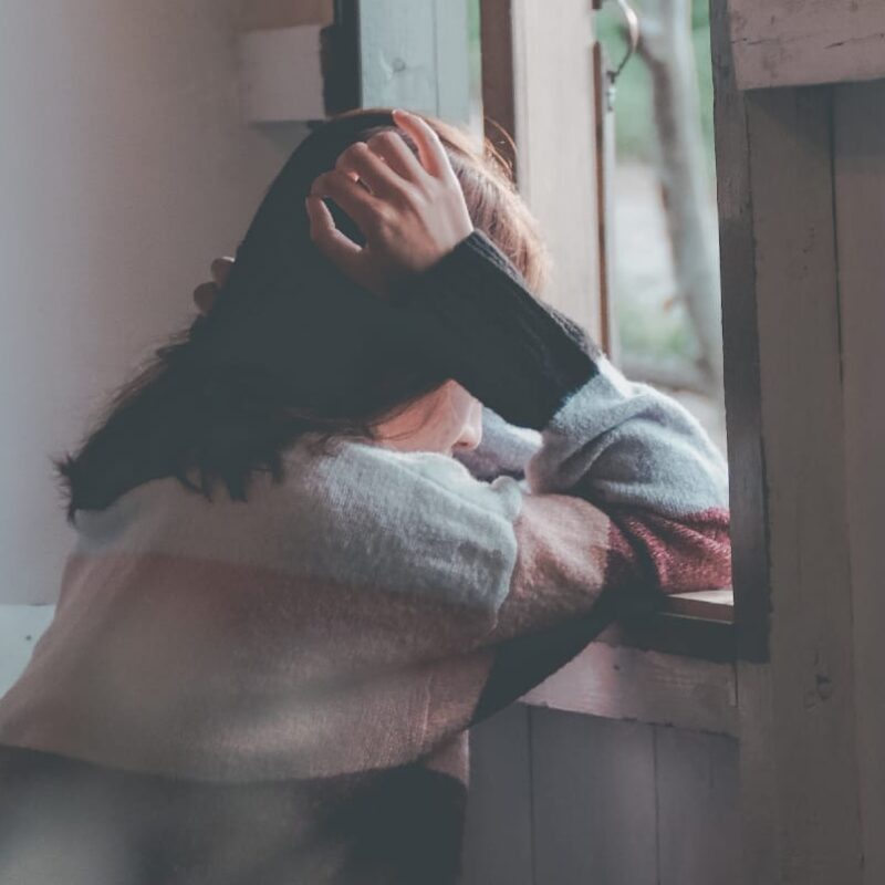 A woman stands by a window, her face showing tears and distress, highlighting the emotional impact of having an alcoholic partner.