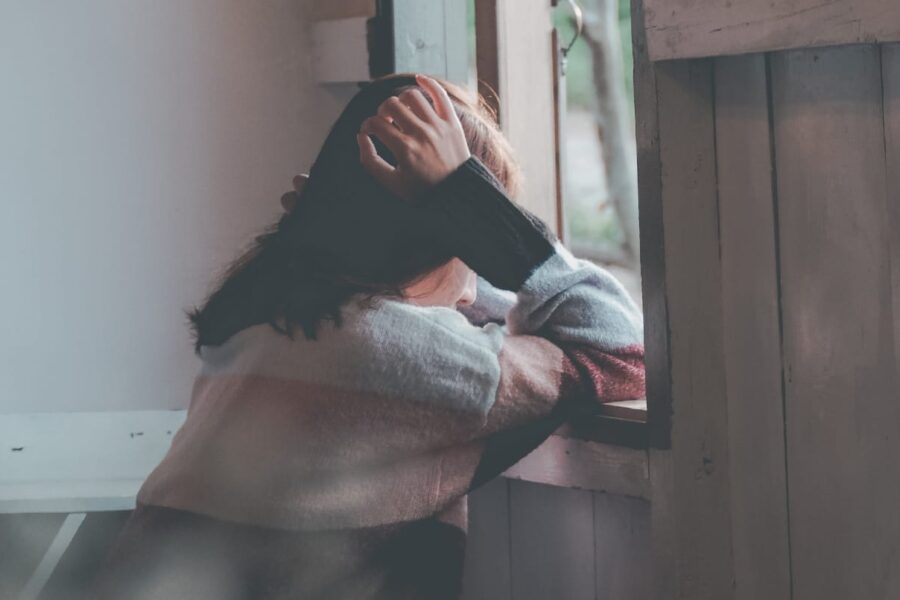 A woman stands by a window, her face showing tears and distress, highlighting the emotional impact of having an alcoholic partner.