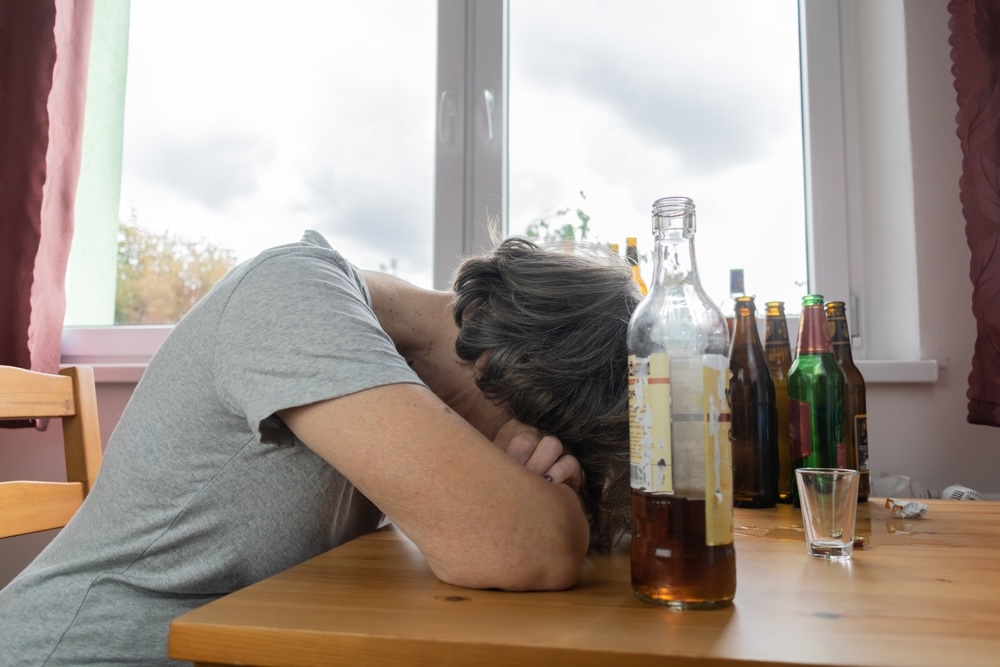 Woman slumped over a table surrounded by empty alcohol bottles